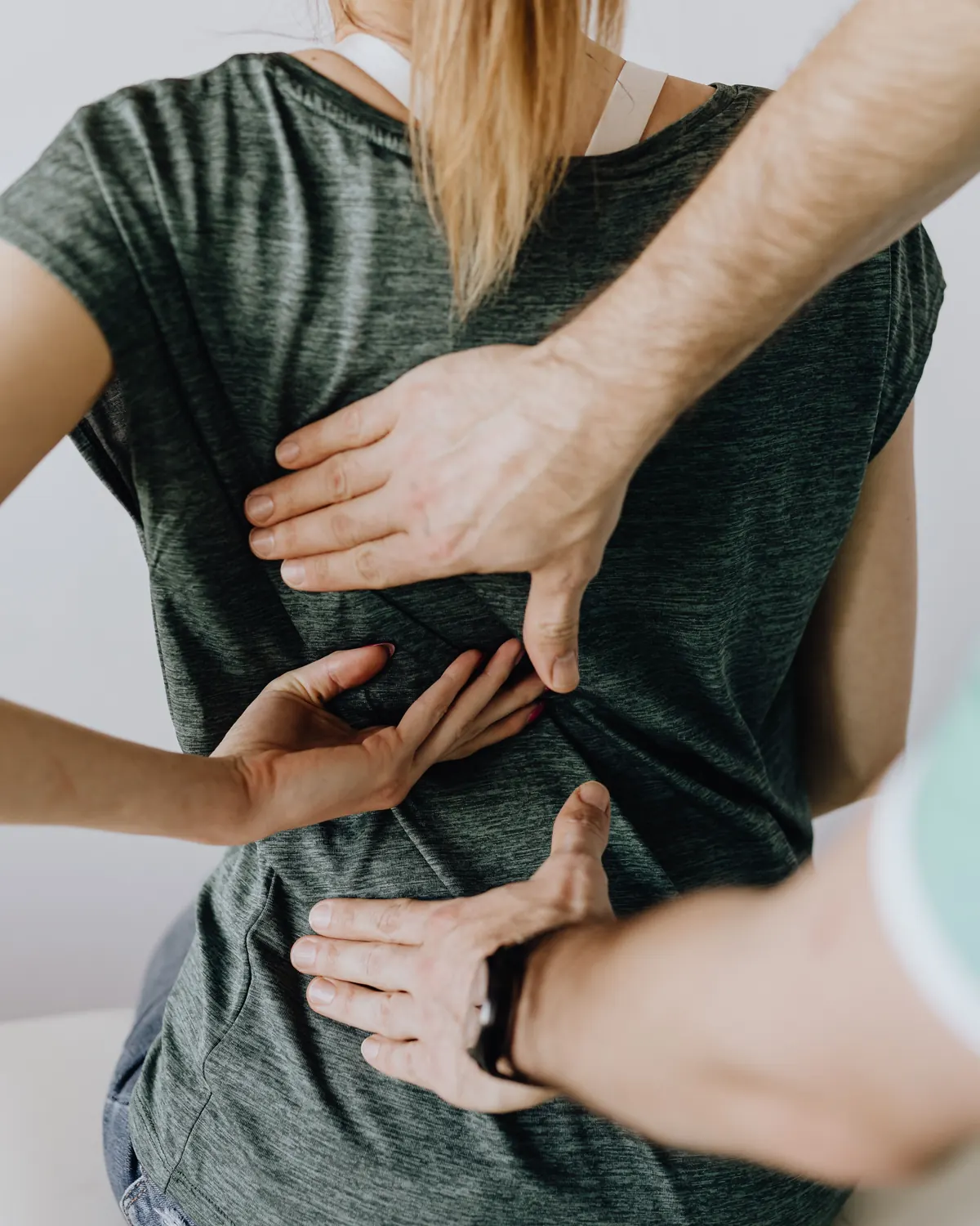 Les mains d’un praticien posées à plat sur le dos d’une patiente assise, qui montre elle-même l’endroit douloureux